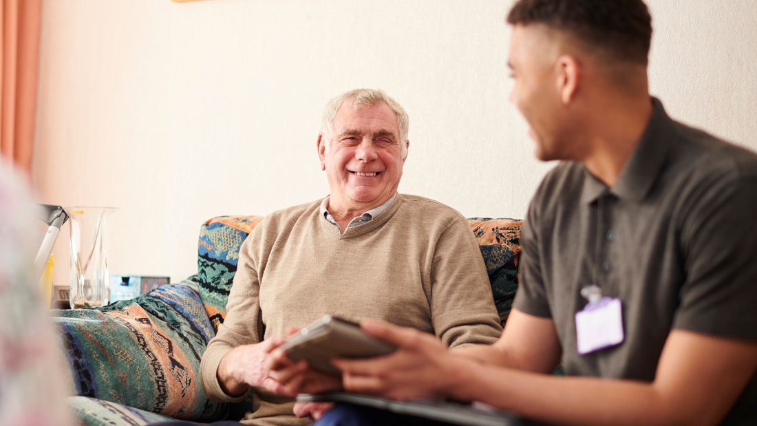 Social Worker smiling at an elderly man, sitting on a sofa