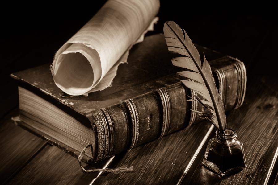 Image of a desk with a leather-bound book, scroll and quill.