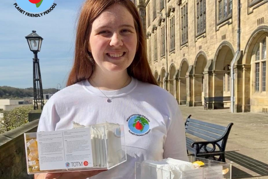 Woman standing in front of Main Arts Bangor Uni building holding sanitary products