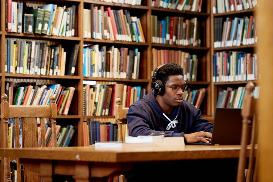 Student in Bangor University library on their laptop with headphones.