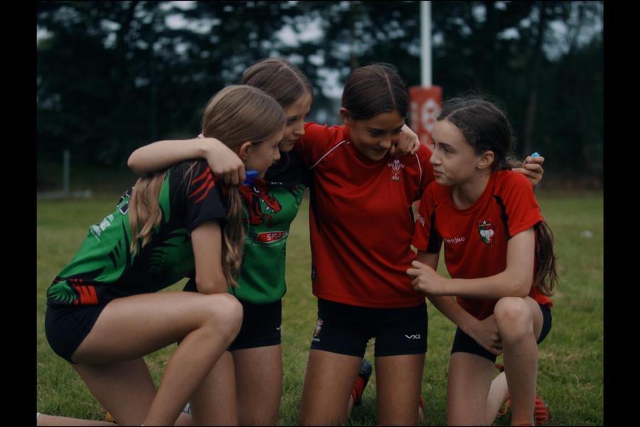A group of 4 young girls kneeling down and discussing tactics before a rugby game 