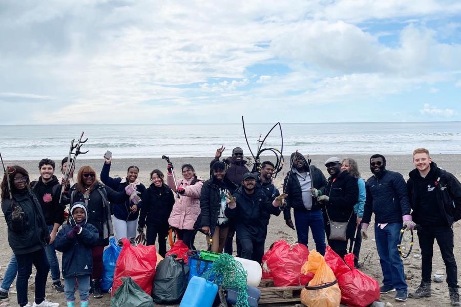 A group made up of International students, staff and children on a beach surrounded by litter bags having recently undertaken a beach clean up 