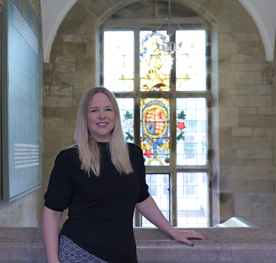 A photograph of Professor Enlli Thomas in front of a stained glass window in the Main Arts Building
