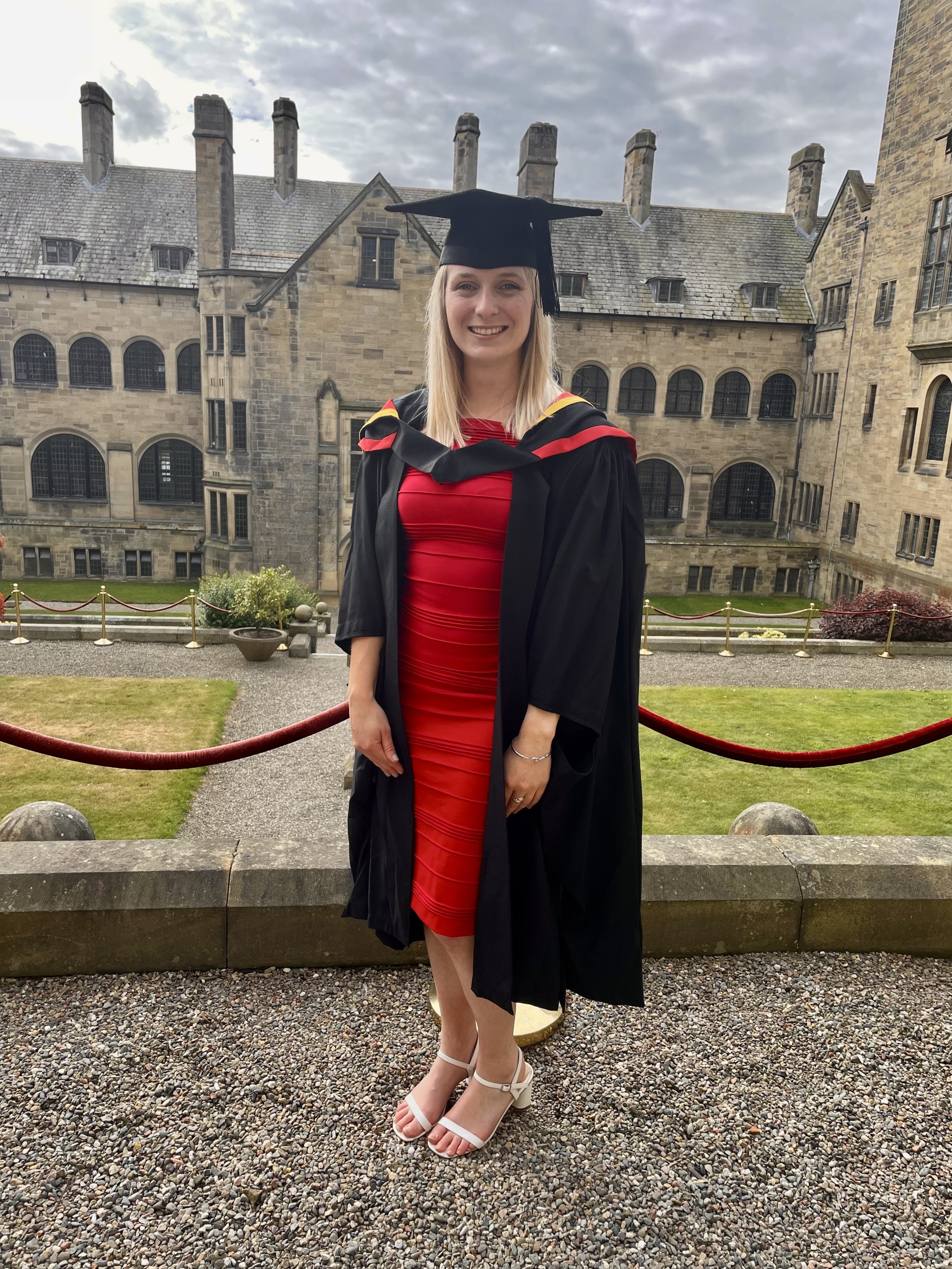 Jennifer outside Main Arts on graduation day in red dress and graduation hat and gown