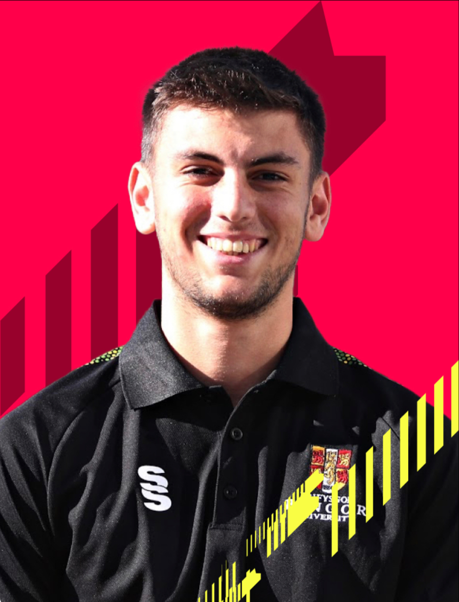 Lewis Thompson looking at camera in Bangor Uni black shirt with red background behind him.