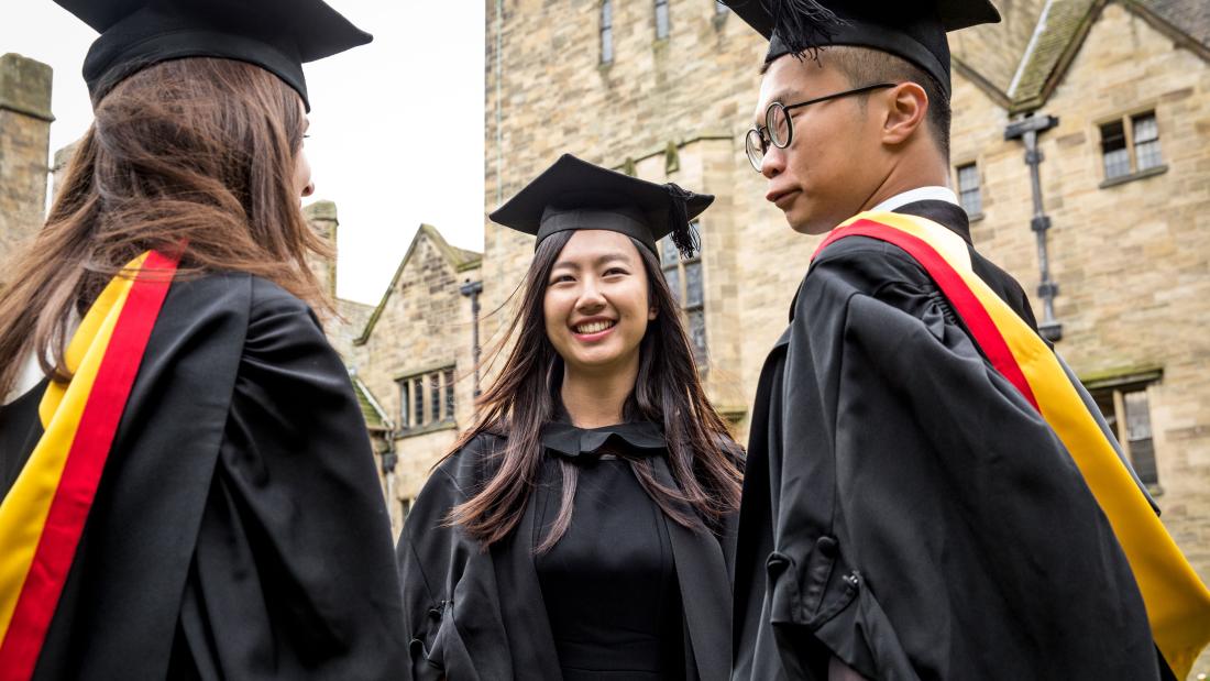 Three students in their cap and gowns outside the Main Arts Building on their graduation day