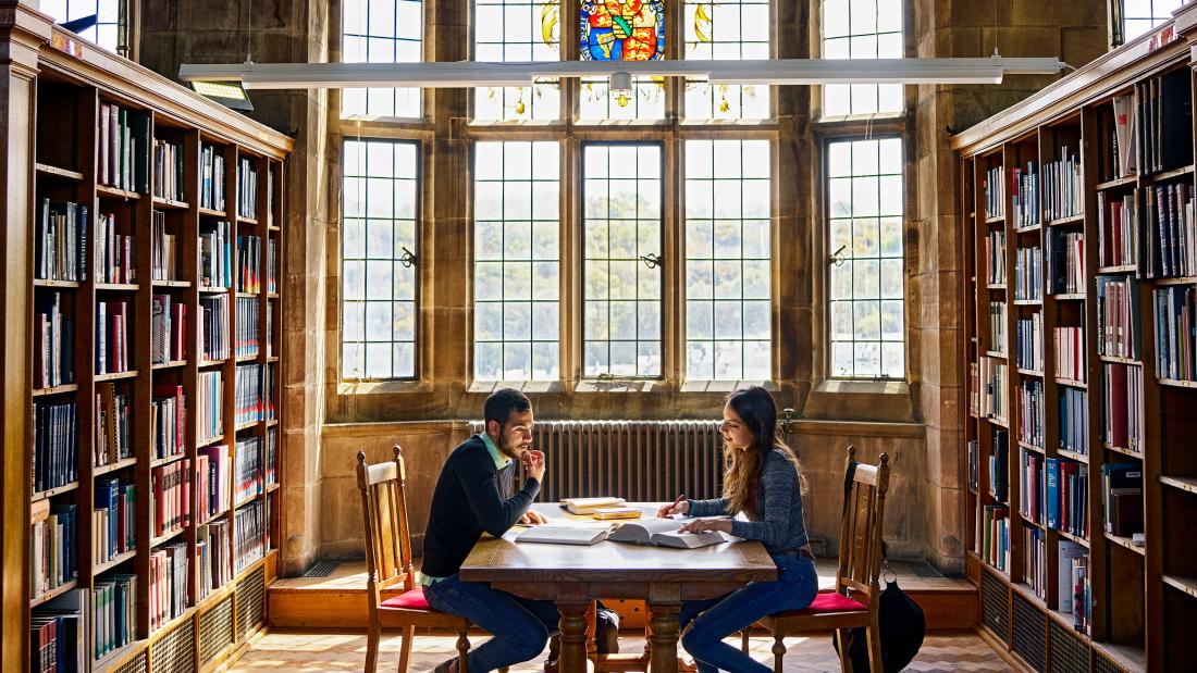 Students working at the Main Arts' Shankland Library with stained glass window in the background