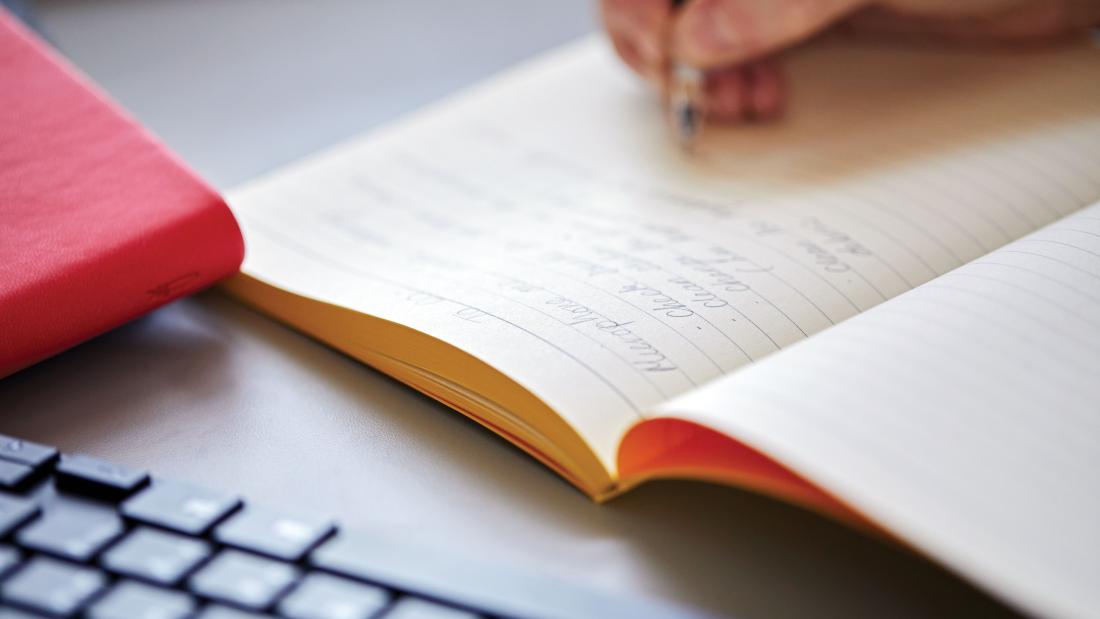 A close up of a student's hand writing notes in a notebook