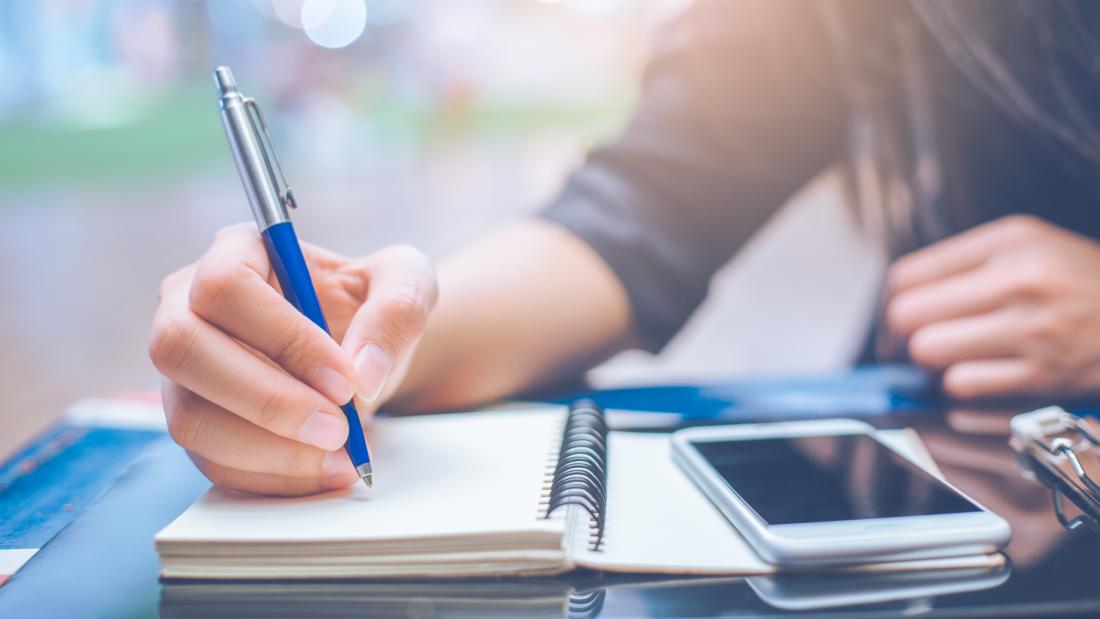 Student at desk with phone and writing.