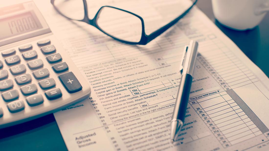 Shows a working desk including accountancy sheet, glasses, calculator and pen.