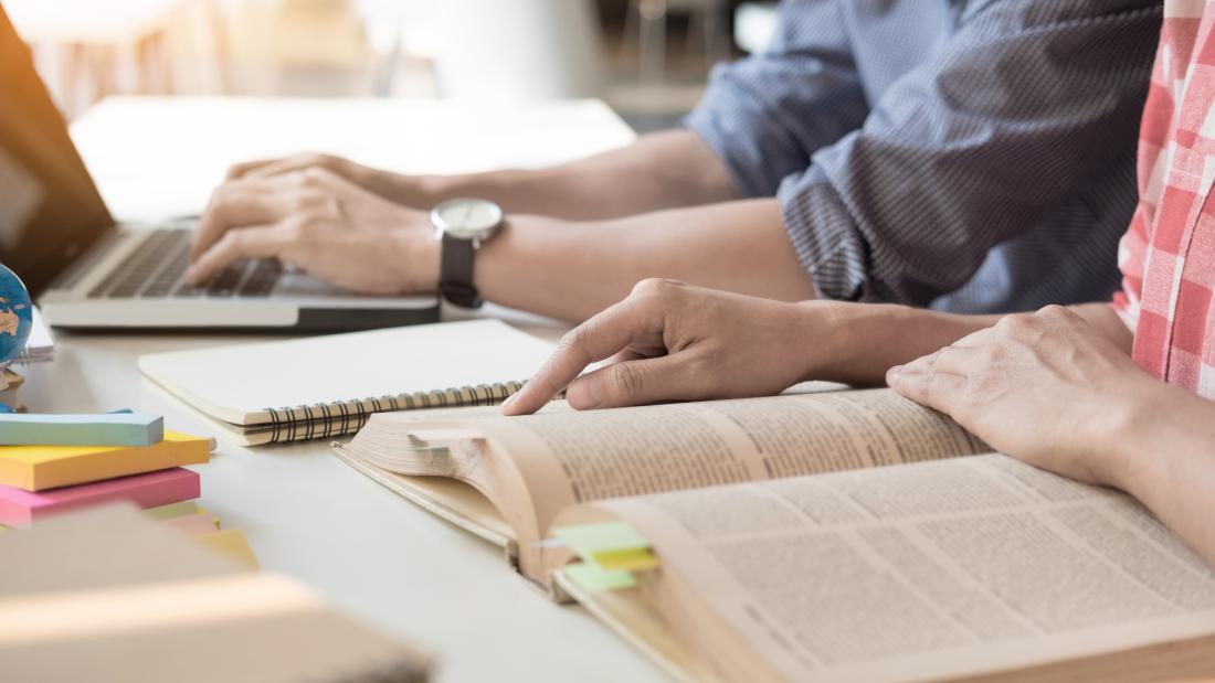 Two students studying together with books and a laptop 