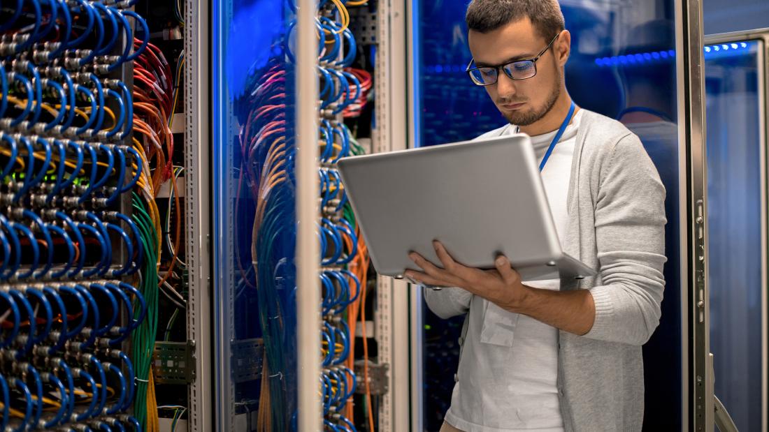  Man holding a laptop standing in server room