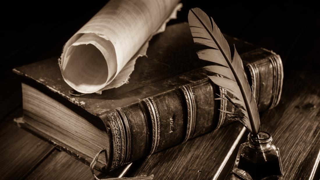 Image of a desk with a leather-bound book, scroll and quill.