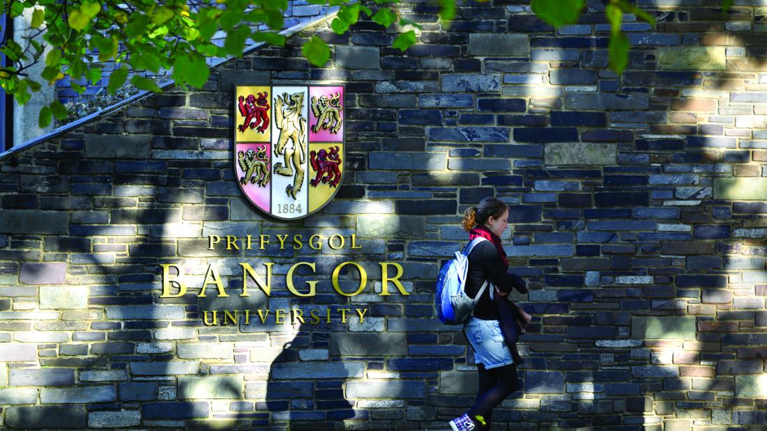 Student walking past the University crest on the wall at main arts