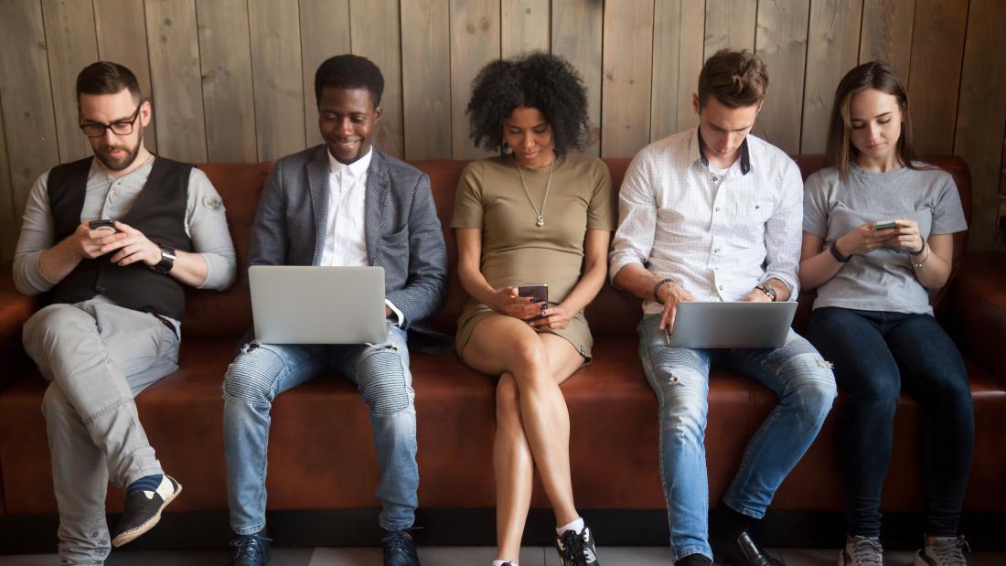 A group of students sitting on a bench using laptops and mobile phones.