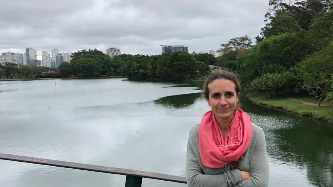 woman looks towards camera with water and cityscape behind