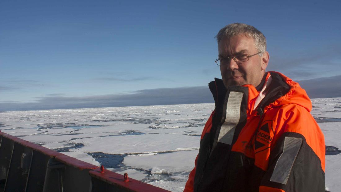 Man on right looks to camera on board a ship, with frozen sea ice in background