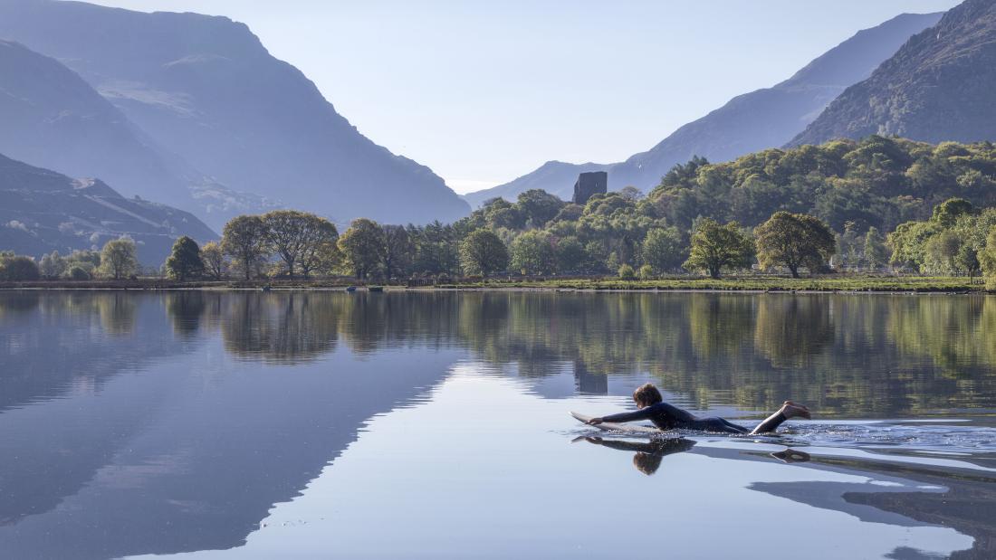 a paddleboarder lies on a paddleboard on Llyn Padarn Padarn Lake with  Snowdonia and the Llanberis Pass as a backdrop