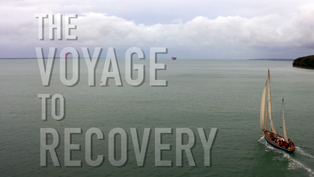 The Voyage to Recovery video screen shot- these words appear to the left of a shot looking down as a sailing boat and some coastline
