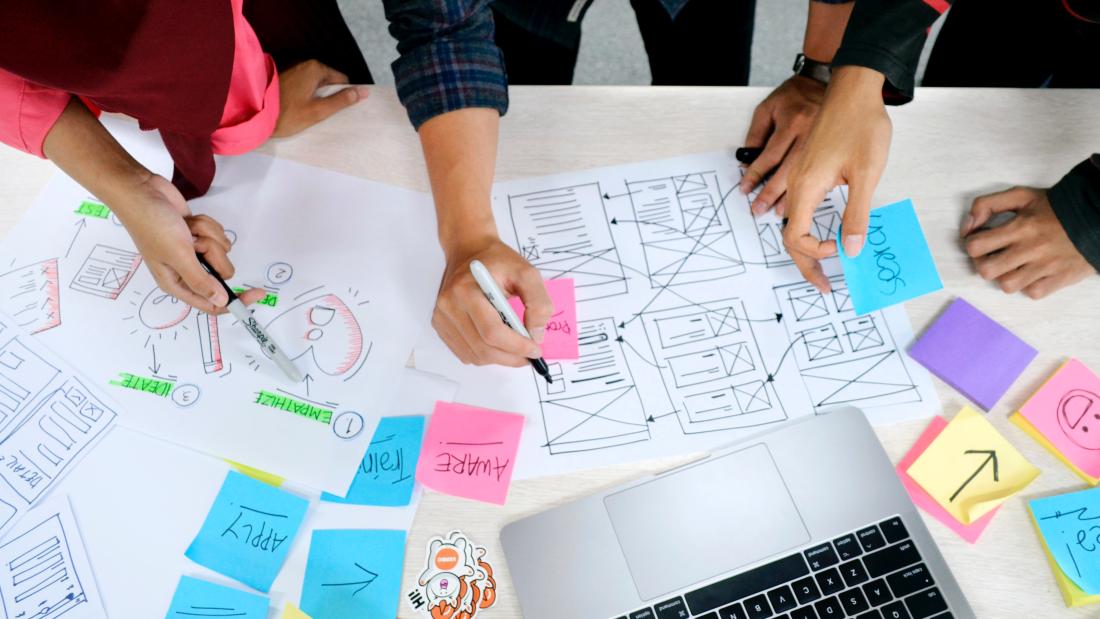 People working on a project on a desk with sticky notes and laptop