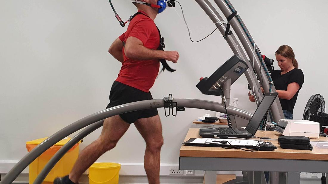 student in a red t-shirt on a treadmill with a mask on his face