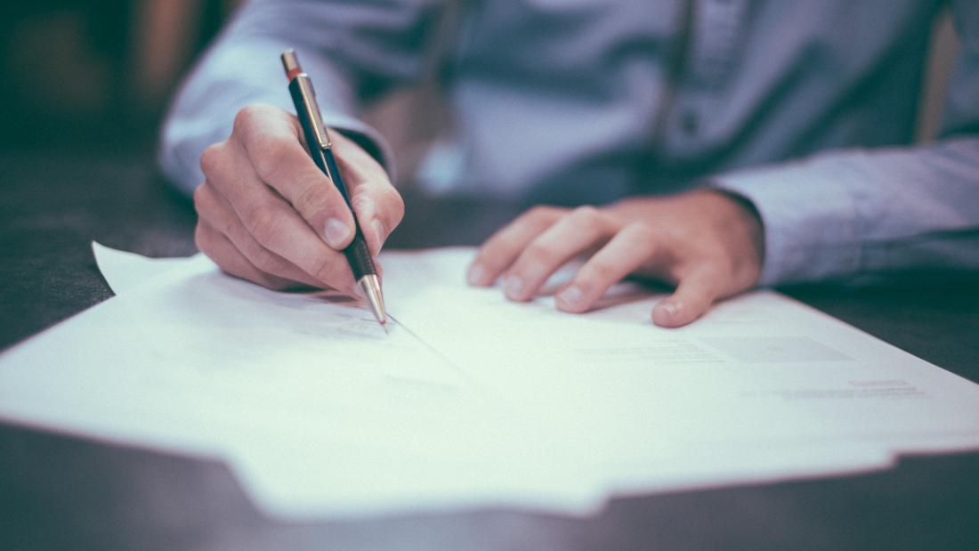 A close up of a man's hands signing a document with a pen