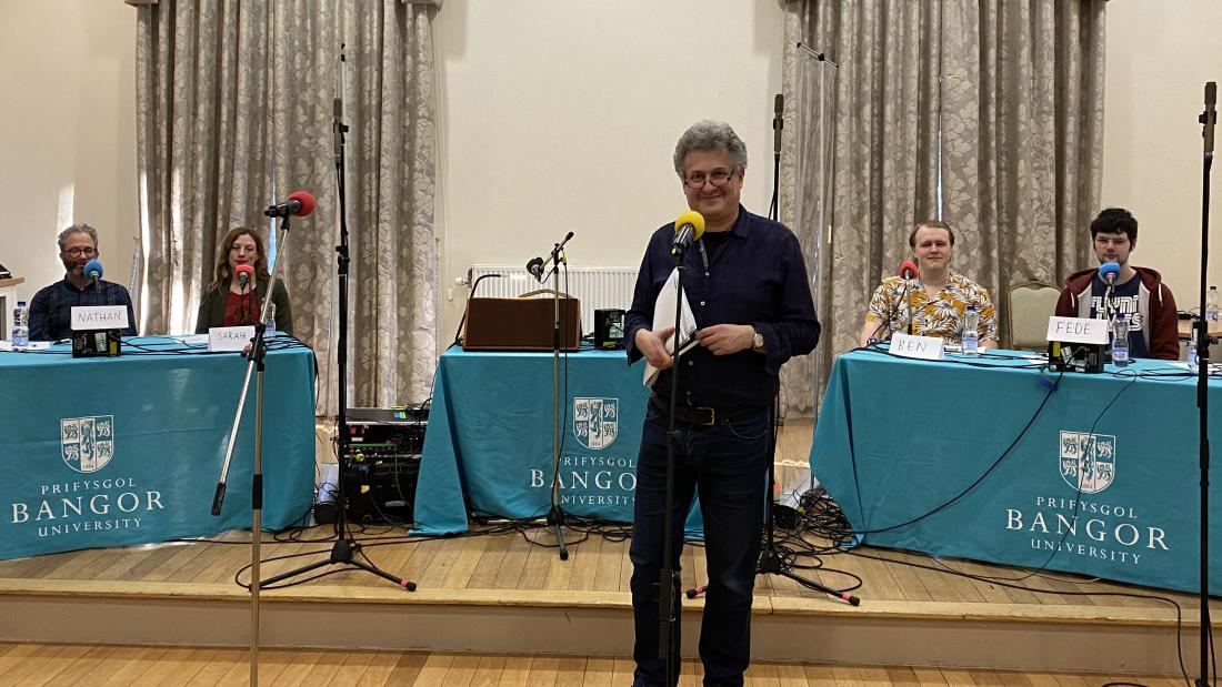 Bangor University 3rd degree Quiz members sit behind tables and microphones ready to compete. In the front is producer, David Tyler.