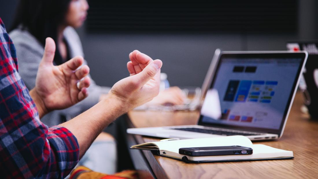 Soeone gesticulates with their hands during an online meeting ( presumably) in front of a laptop computer screen. 