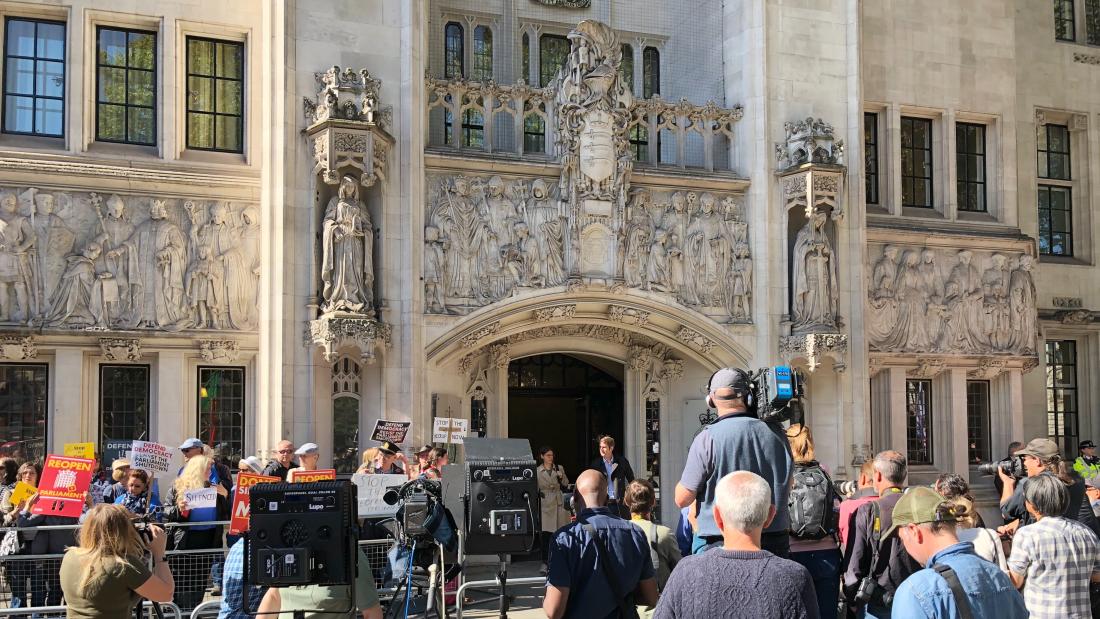 The backof a crowd of media outside an ornate building.