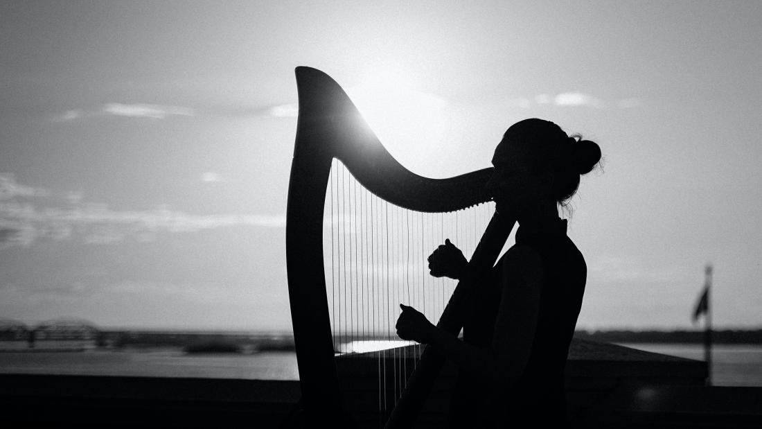 Black and white photo of a woman playing a harp outside