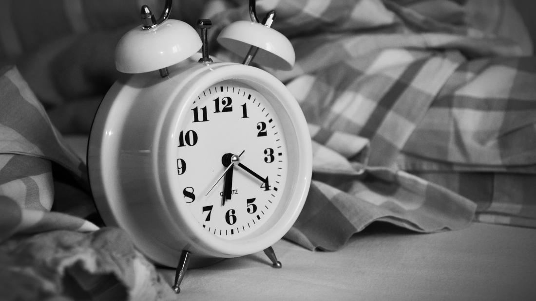  a black and white image of an old fashioned type of alarm clock next to a bed, the time is 6.20