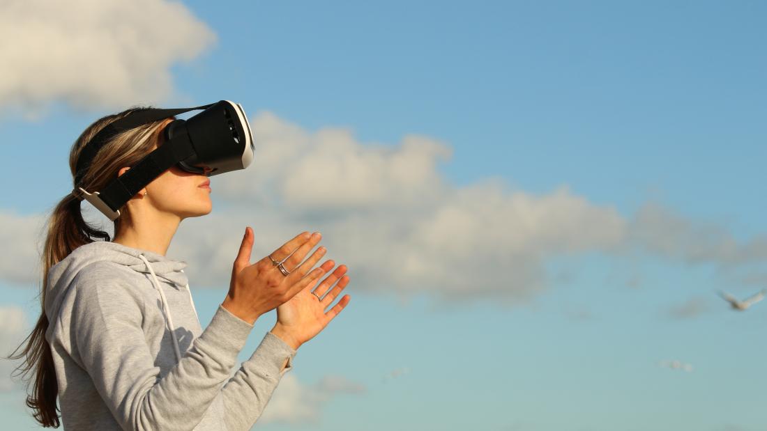 Woman wearing virtual reality headset with blue sky and white clouds in the background