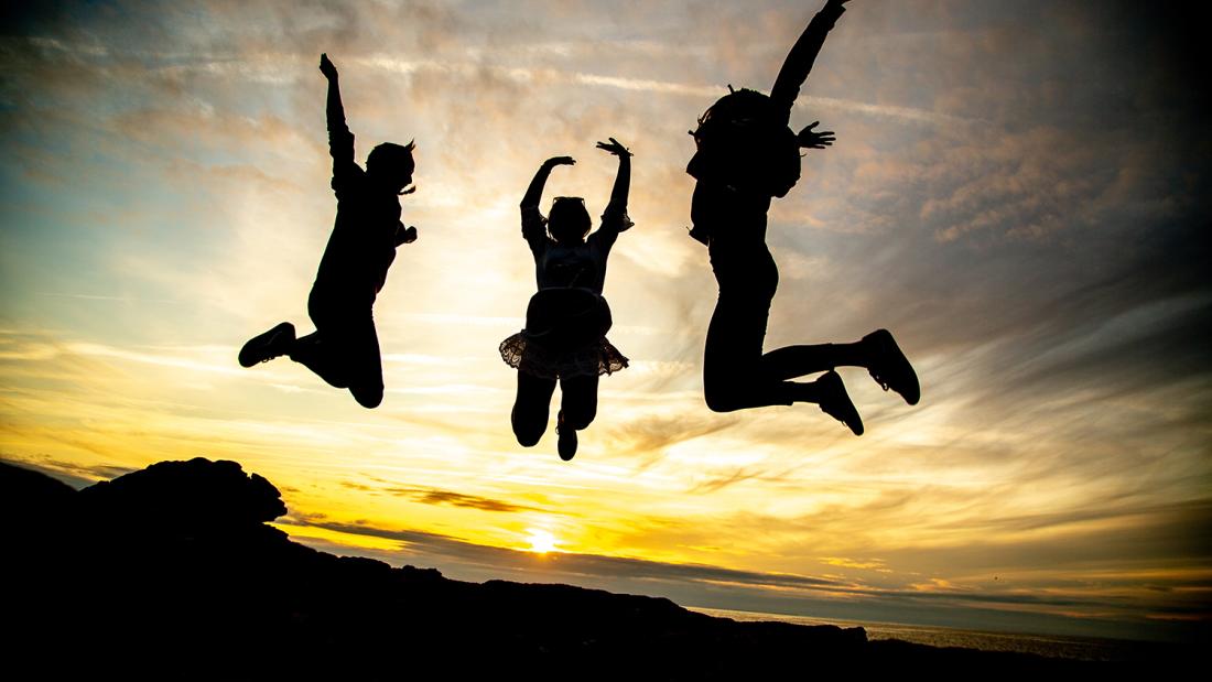 Three people jumping up, with a sunset in the background