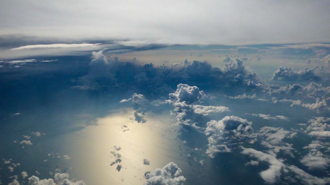 Aerial view looking down at clouds over the sea with sunlight reflected from below