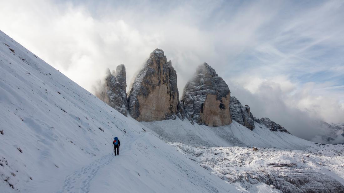 A landscape image of a mountain with three peaks, covered in snow and a person walking towards the summit 