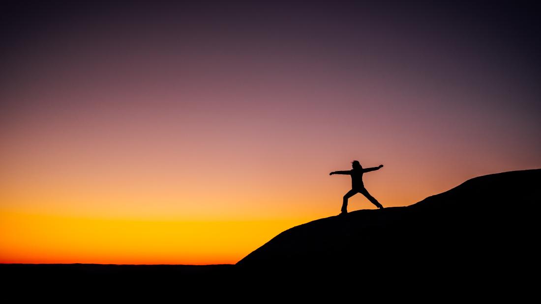 a person doing yoga on a mountain whilst the sunis rising