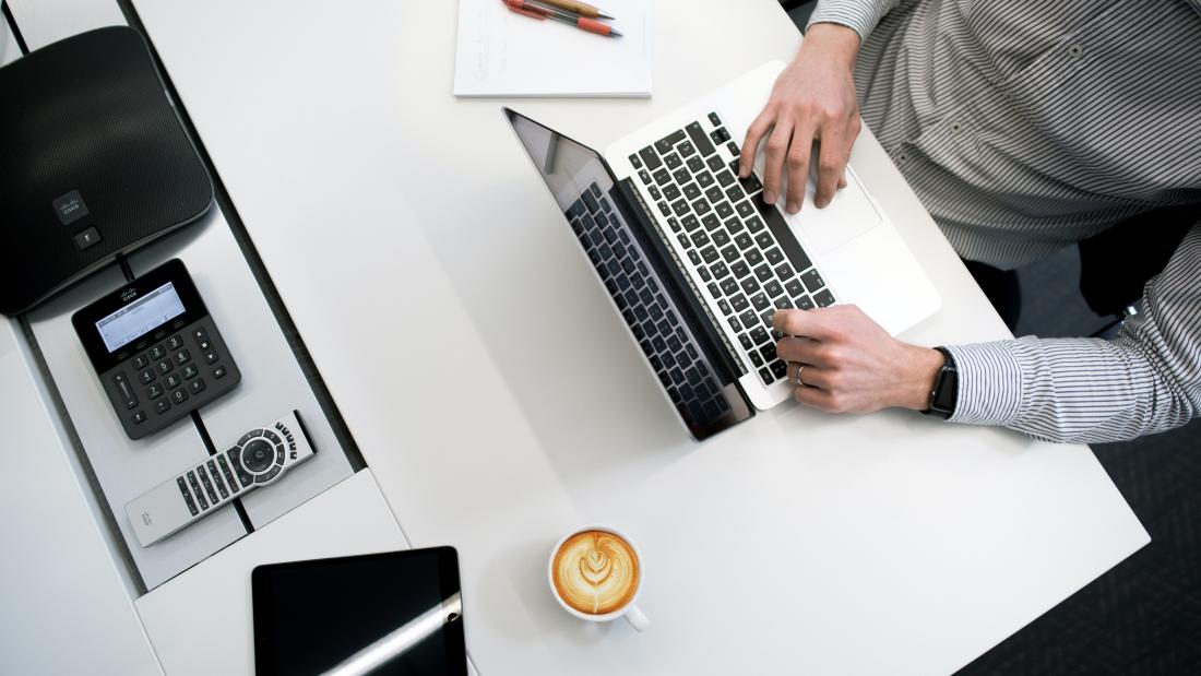 Someone sitting at a desk typing away at a laptop
