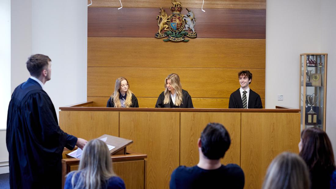 Student brings his case to the mock moot courtroom where three other students act as judges sitting behind the desk in front of audience. 