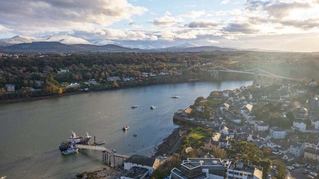 The School of Ocean Sciences photographed from the air with the suspension bridge behind and snowy mountains of Snowdonia in the distance