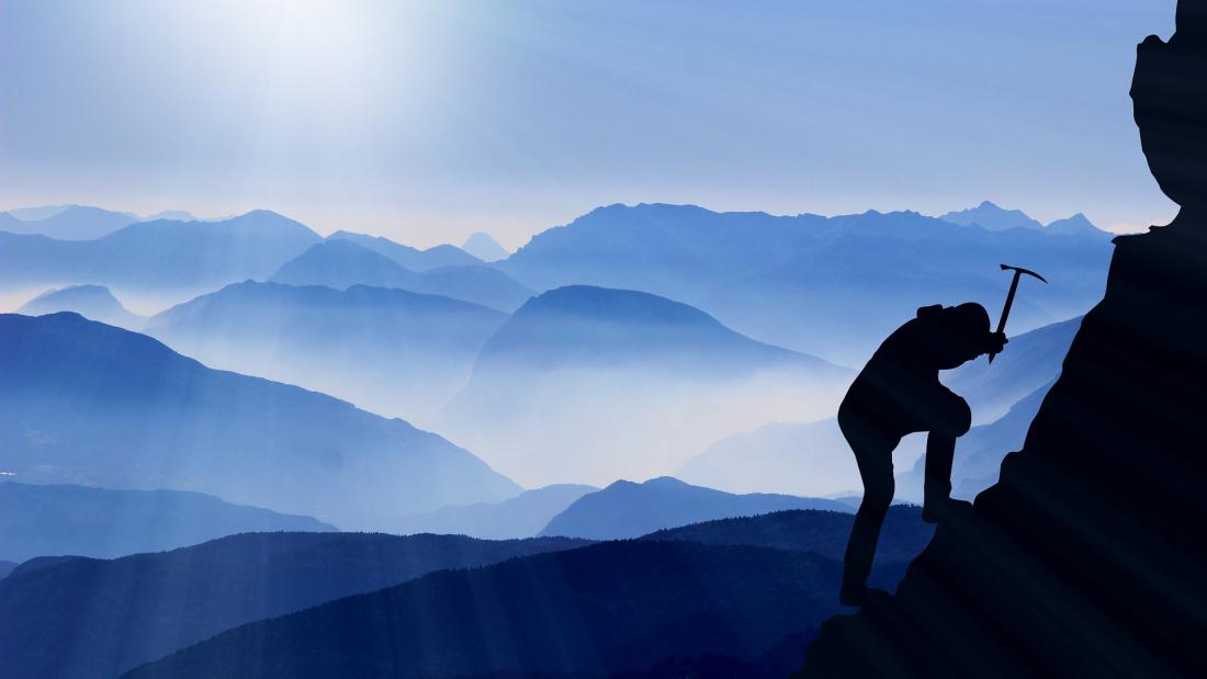 A silhouette of climber wielding an ice pick. In the background are many misty mountain-tops in varying shades of blue