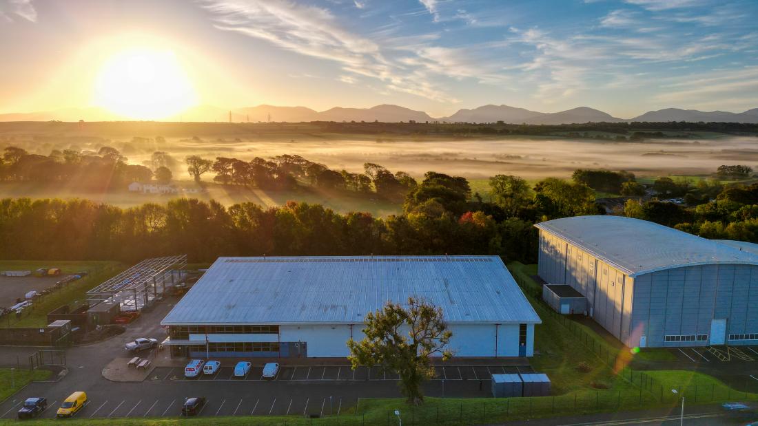 Aria Flm Studios in the foreground with a sunrise over a pastoral setting and mountains in the background