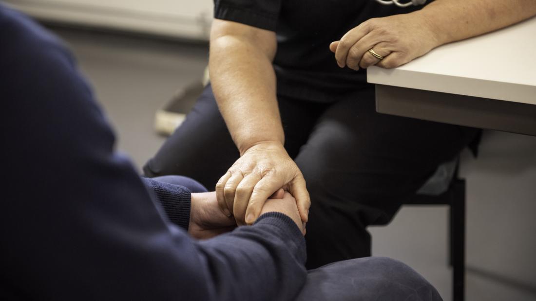 A close up of a doctor (stethoscope seen hanging from neck), places hand over patient's clasped hands.