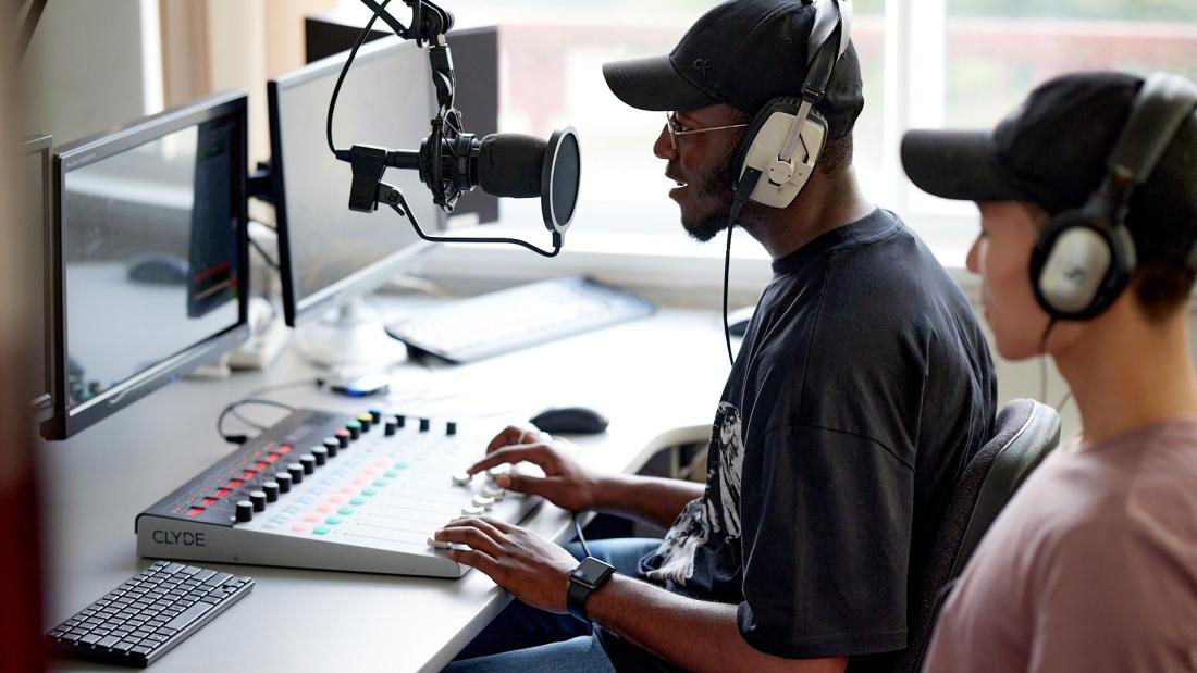 Two students sitting at a desk using podcast recoding equipment