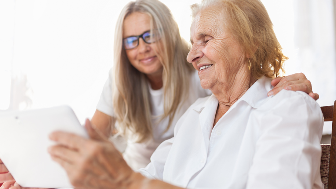 Younger member of family with an elderly member, looking at a tablet screen