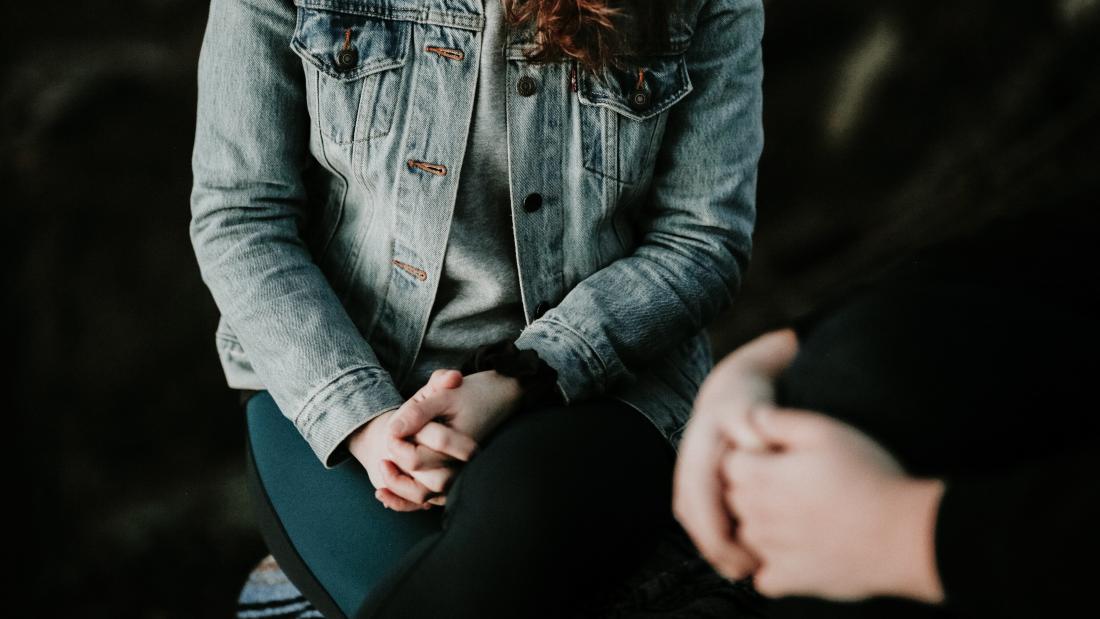 Image of a person sitting down with their hands clasped 