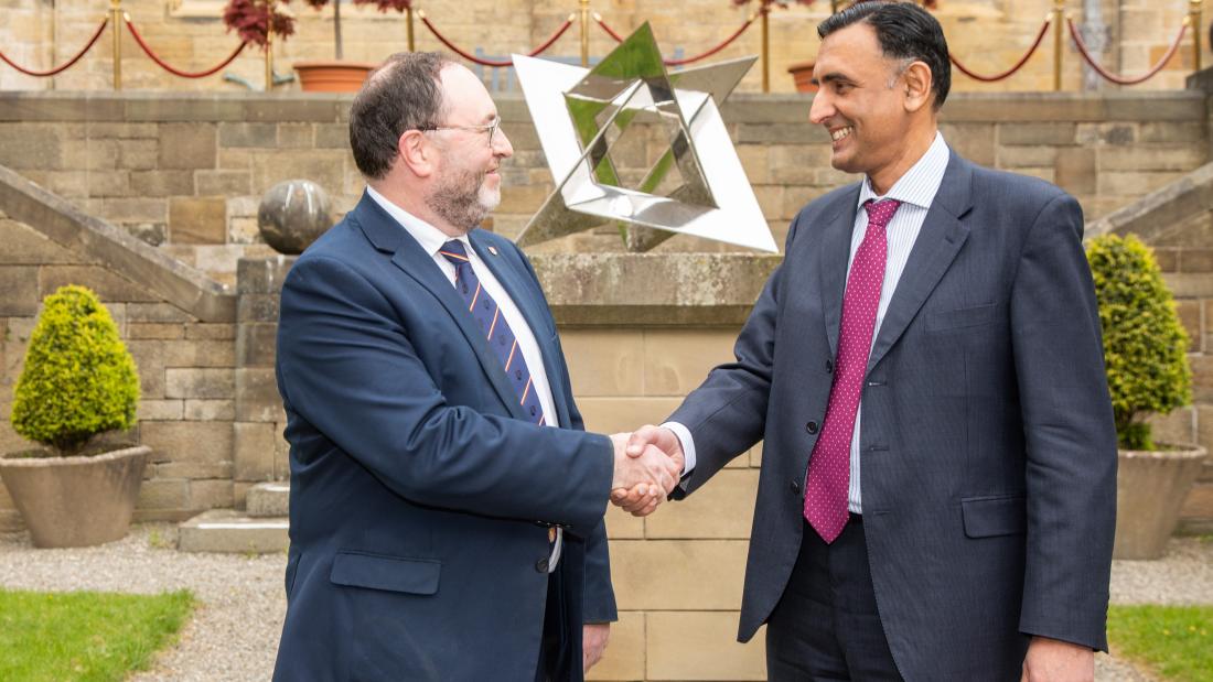 Two people shaking hands in front of a courtyard