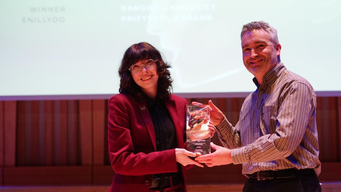 Person in red suit and black shirt accepting an award on stage