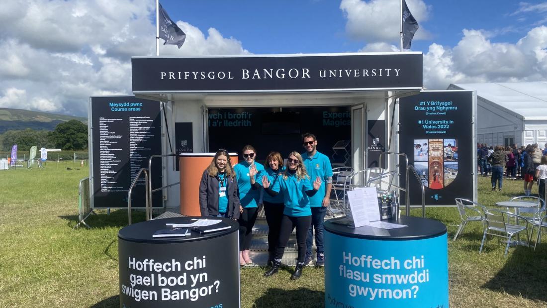  Stand Prifysgol Bangor efo pobol yn sefyll y tu allan 