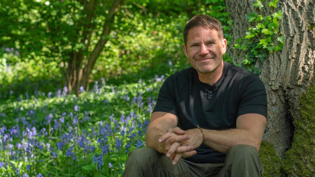 Steve Backshall sits outside surrounded by bluebells and a background of trees