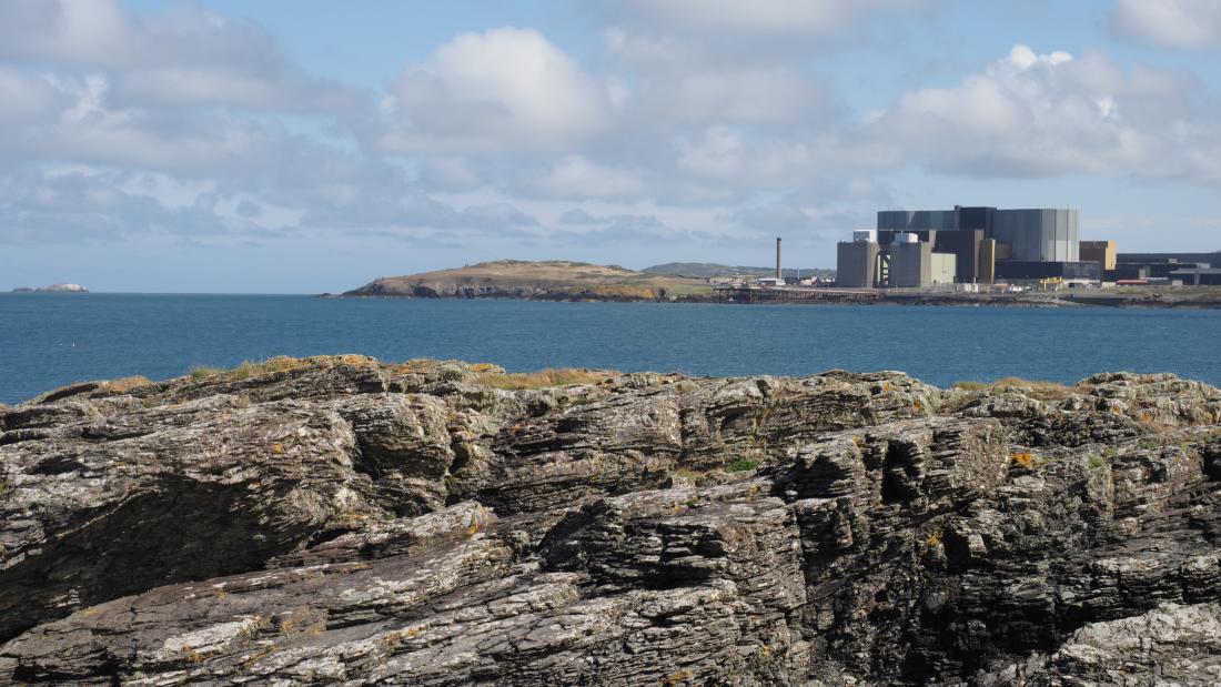 Gorsaf Ynni Niwclear Wylfa o Fae Cemaes ar Ynys Môn, gyda chreigiau yn y blaendir